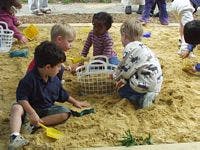 Four children playing in a sandbox with toys