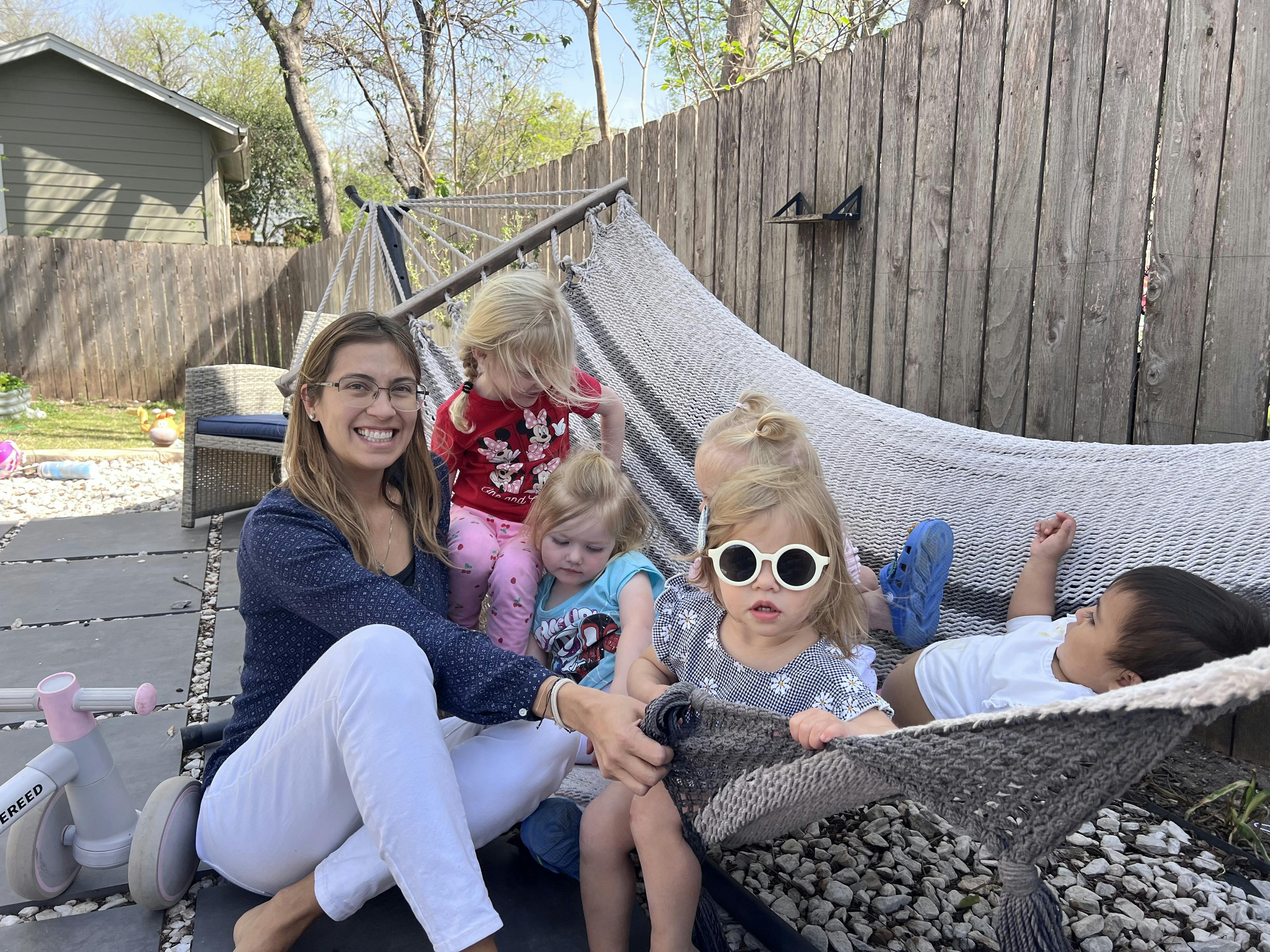 Person and multiple children sitting around a hammock outdoors