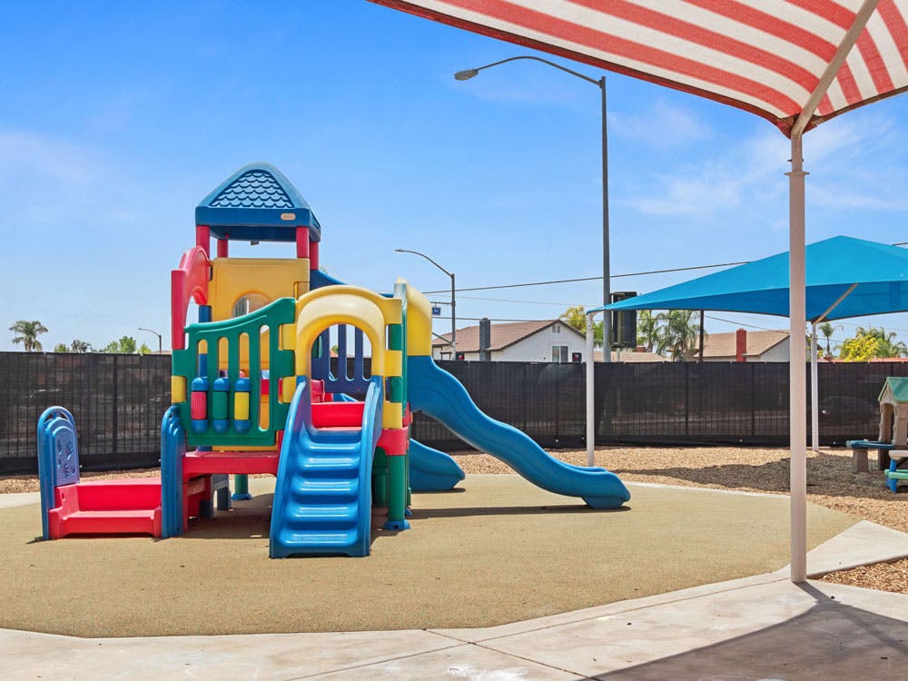 Colorful playground with slides, stairs, and play structure under a red and white canopy