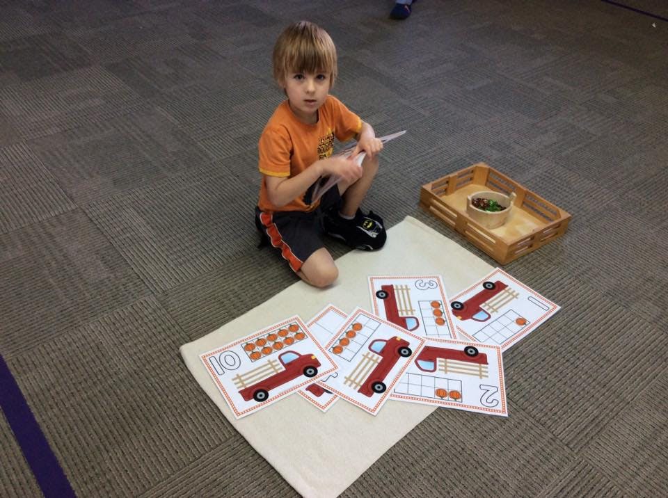 Child kneeling on floor with number cards and small objects