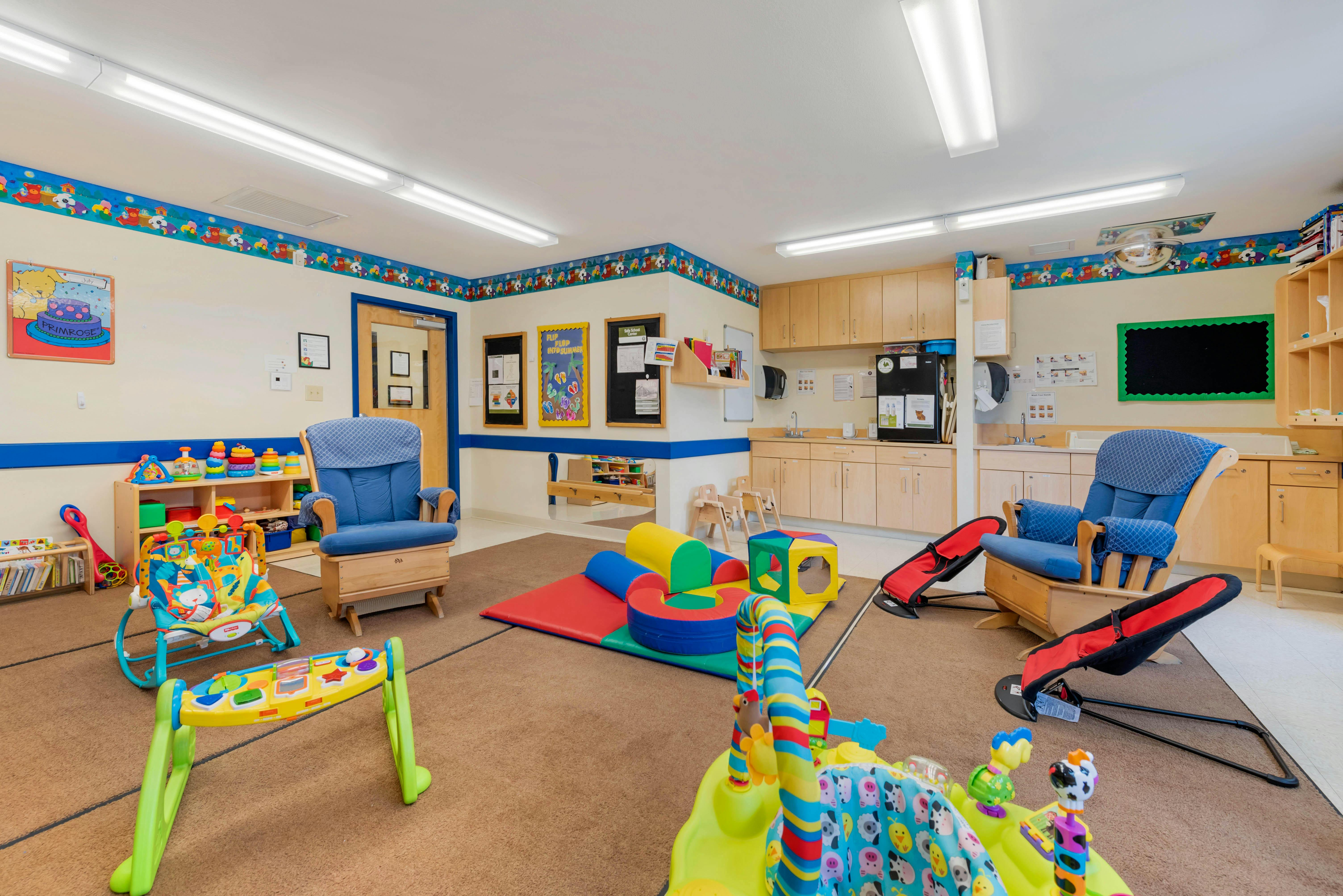Playroom with colorful baby toys, two blue rocking chairs, and a kitchen area