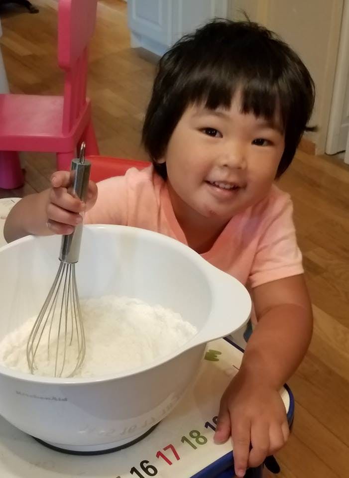 Child holding a whisk in a bowl of flour