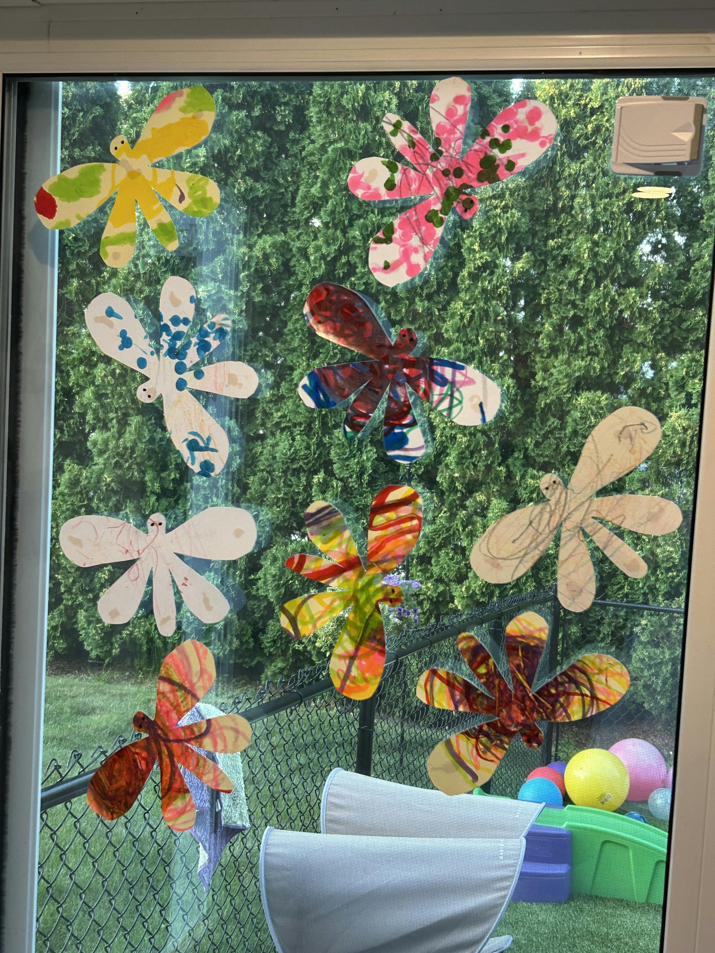 Paper cutouts of flowers and dragonflies on a window