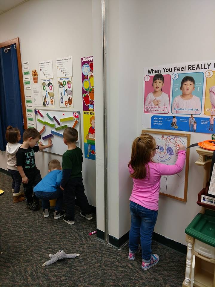 Children playing with toys on a wall and drawing on a whiteboard