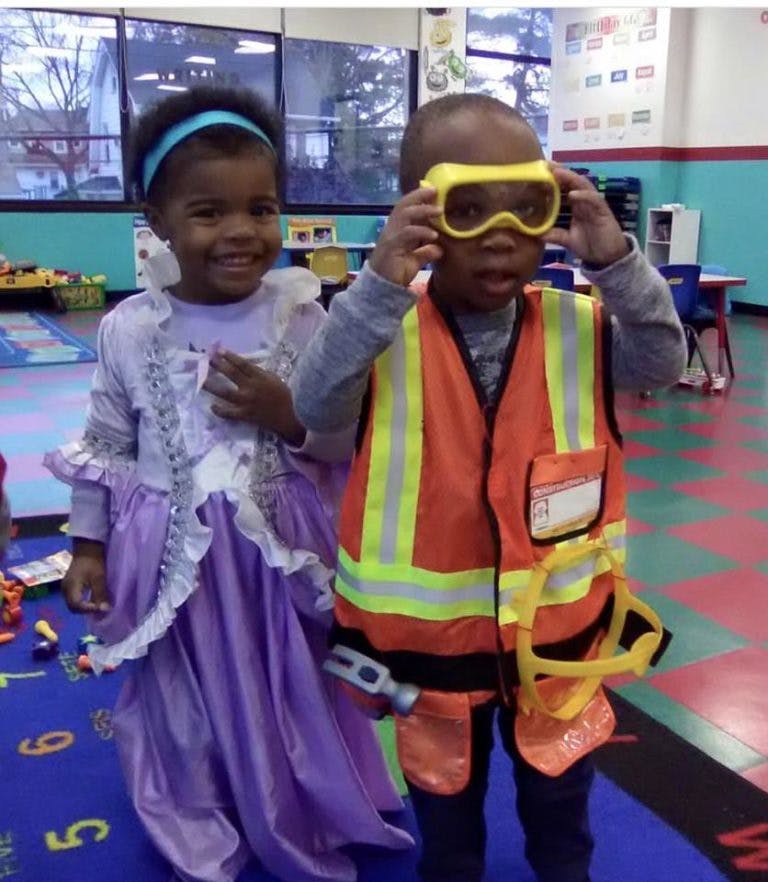 Child in purple dress next to child in construction vest and goggles