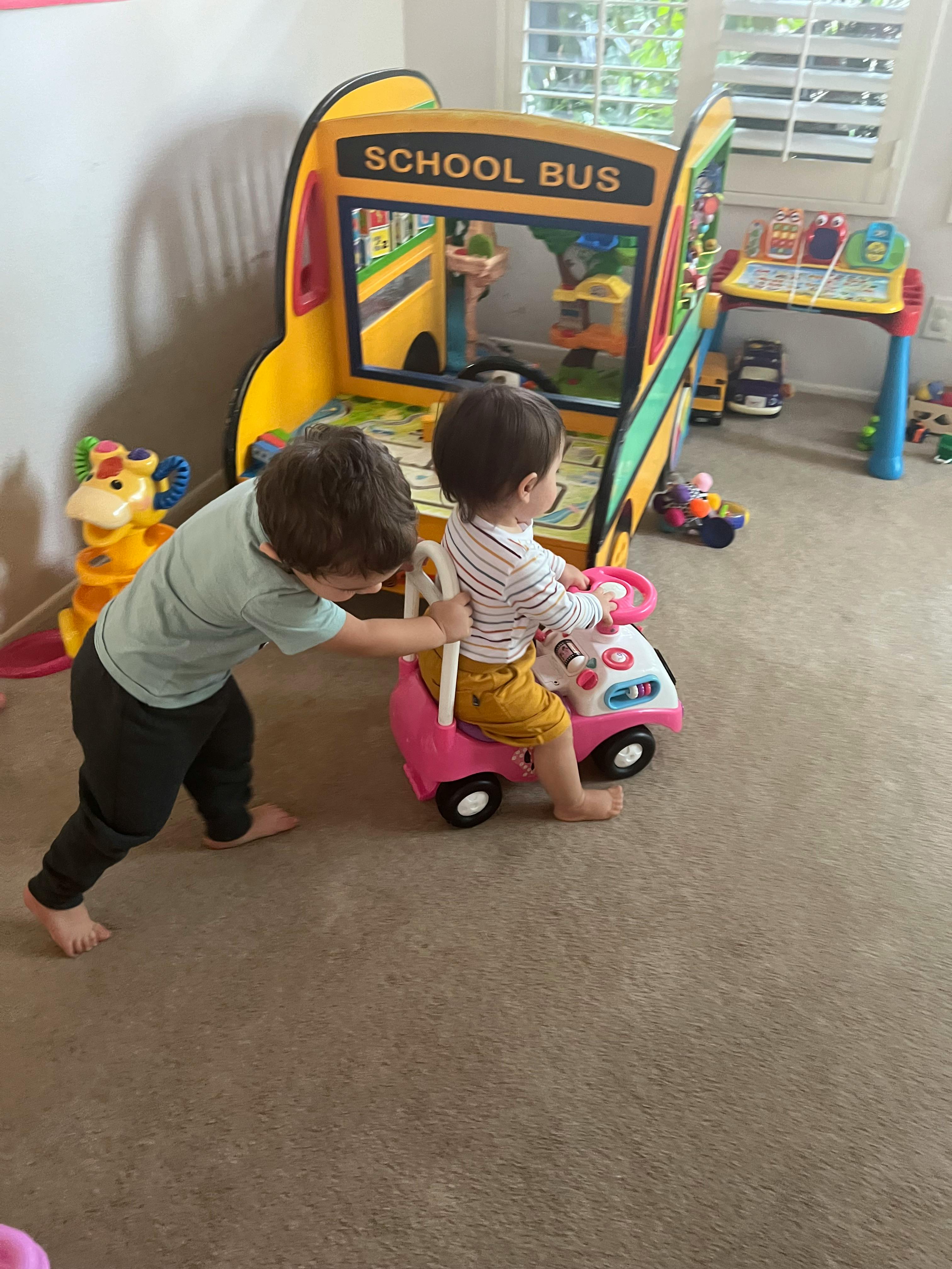 Child pushing another child in a toy car in a play area