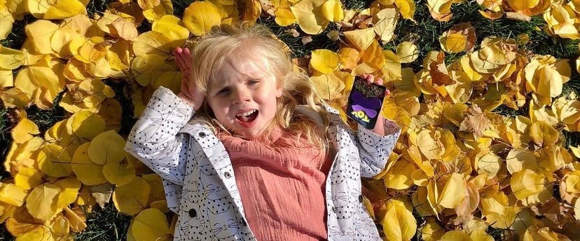 Child lying in yellow leaves holding a small object