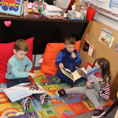 Three children sitting on a rug and reading books