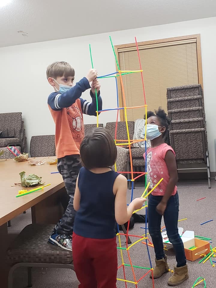 Three children building a structure with colorful sticks and connectors