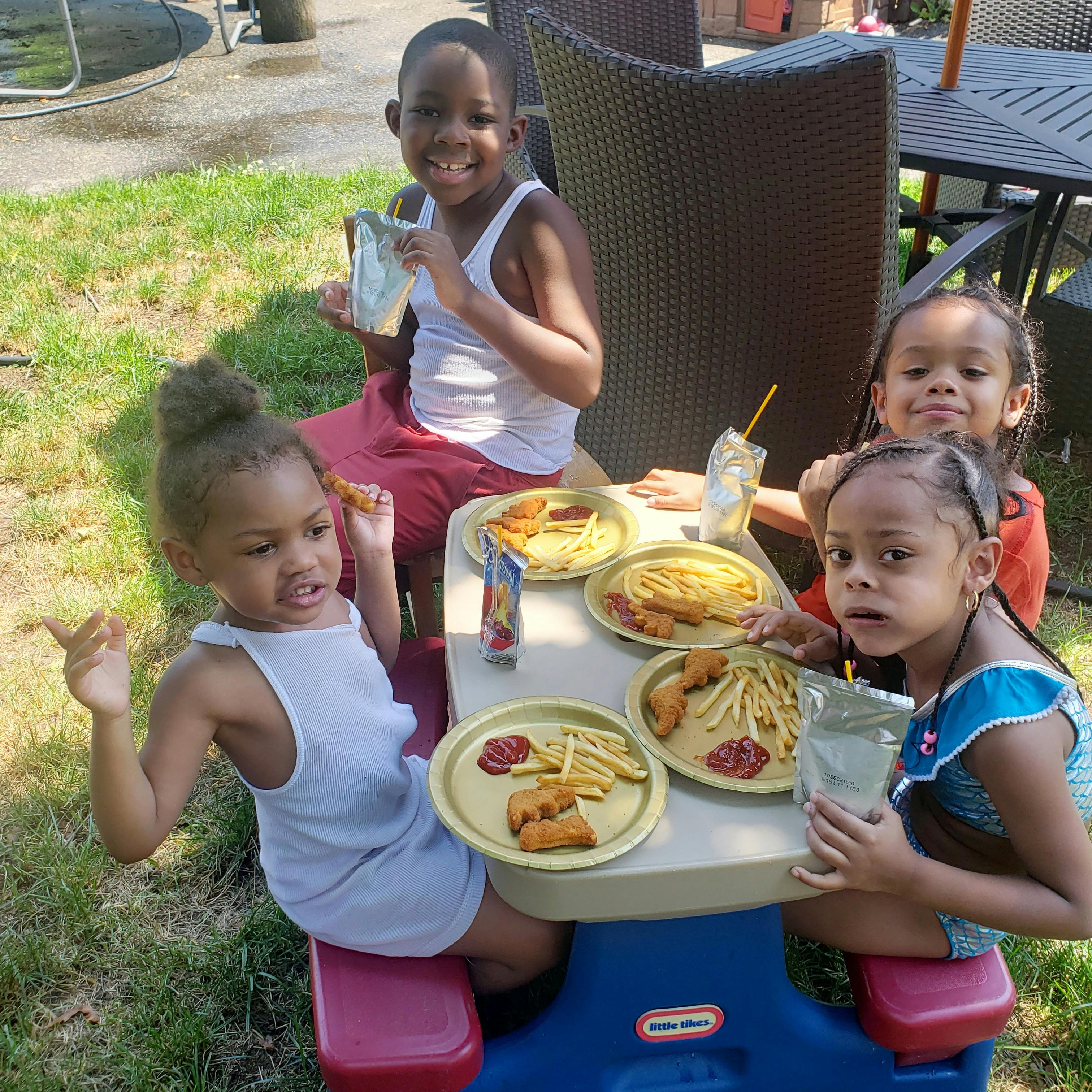 Four children eating at a small table outdoors