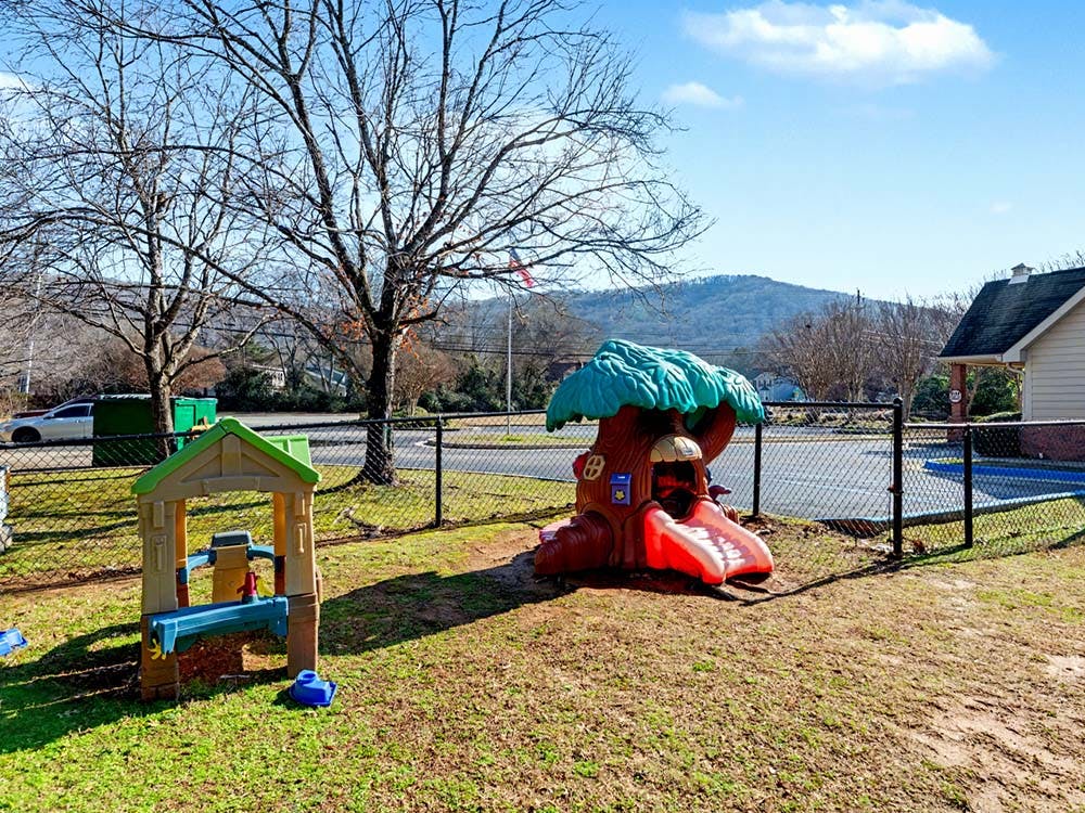 A fenced playground with a tree-themed playhouse and a plastic activity table