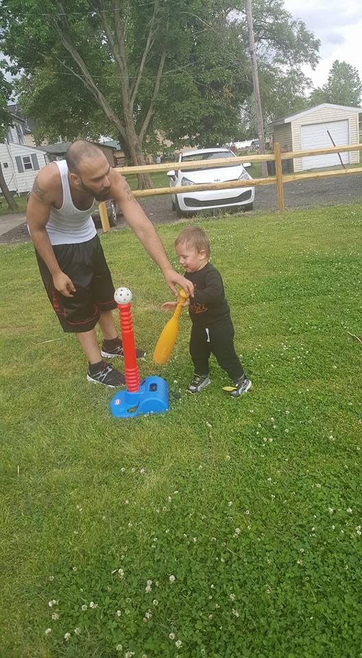 Person helping a child with a toy baseball bat and tee ball stand