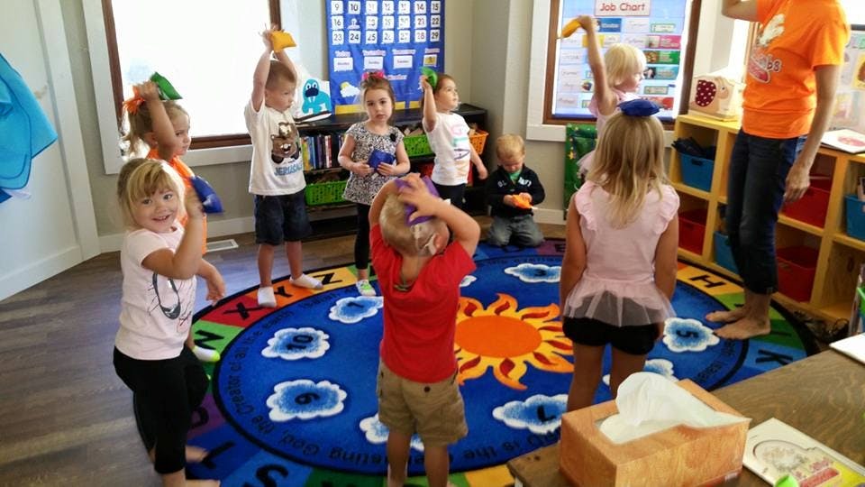 Children standing in a circle on a rug, some holding objects above their heads