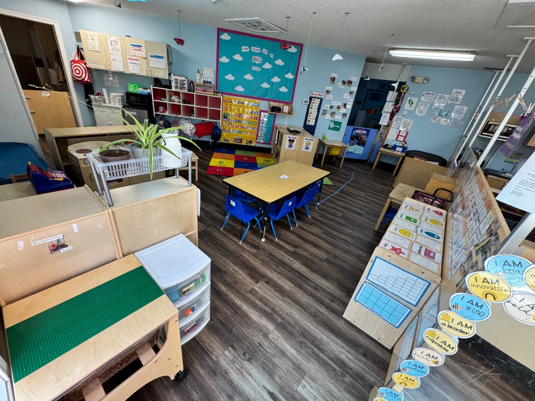An empty children's classroom with small tables, chairs, and learning materials