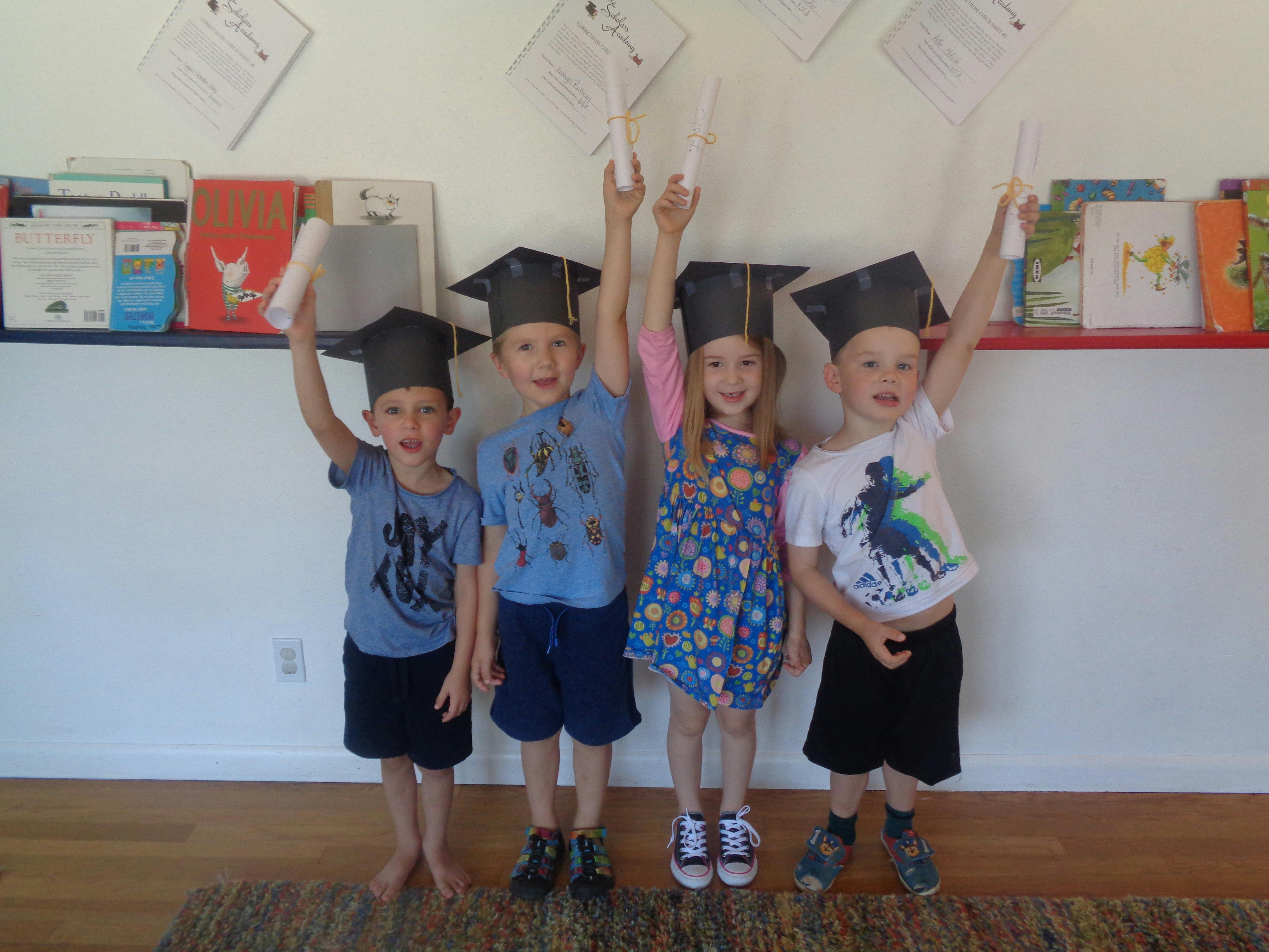 Four children wearing graduation caps and holding up diplomas