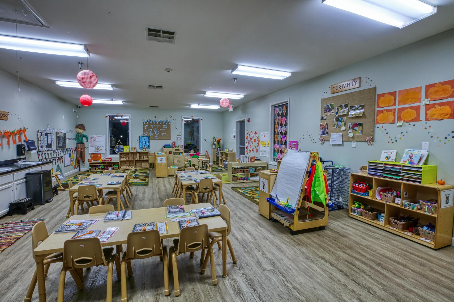 An empty classroom with child-sized tables and chairs, artwork on walls
