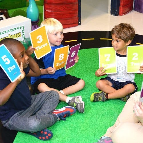 Three children sitting on a green mat holding up number cards