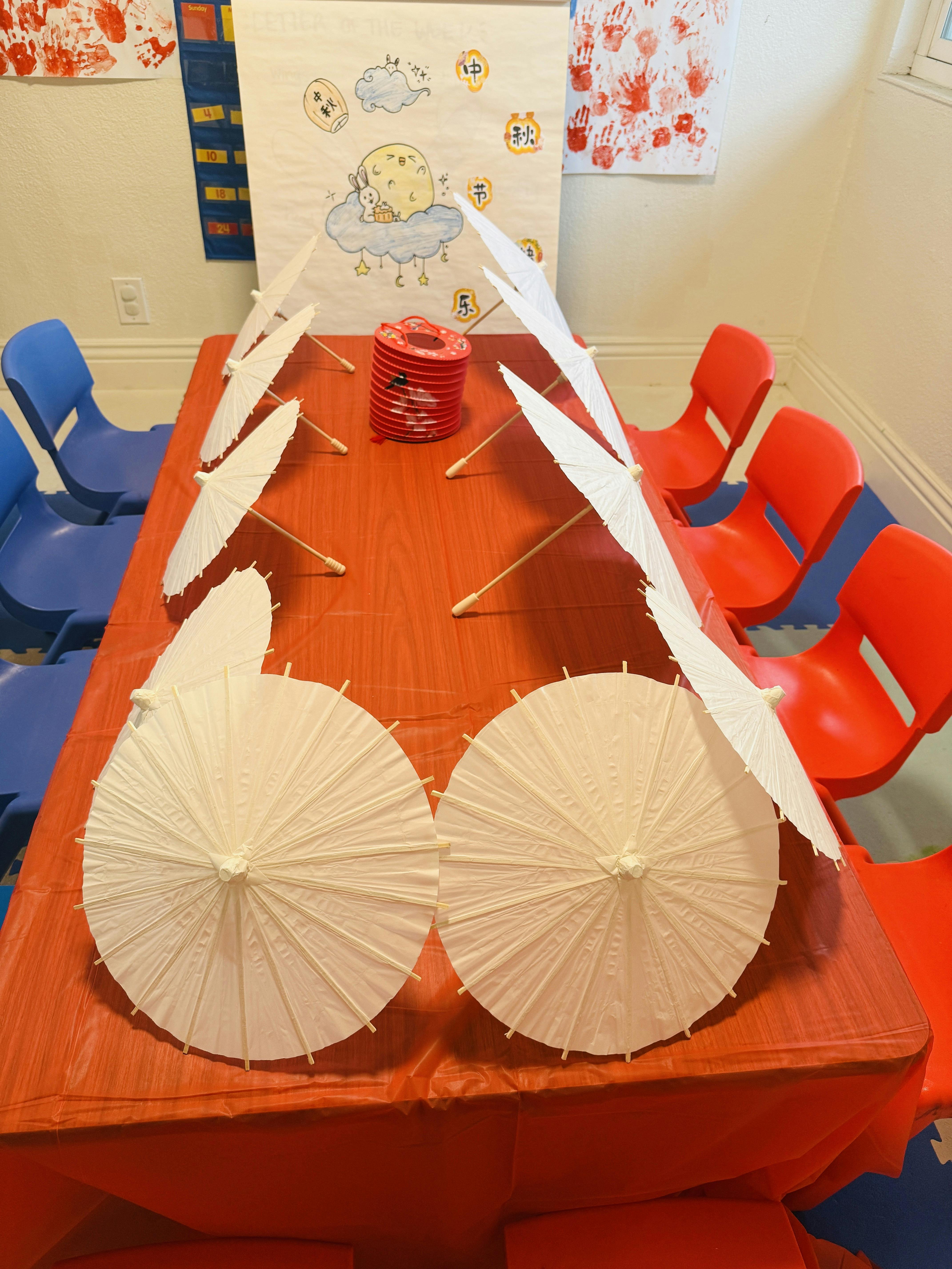 White paper umbrellas and a red lantern arranged on a table in a classroom