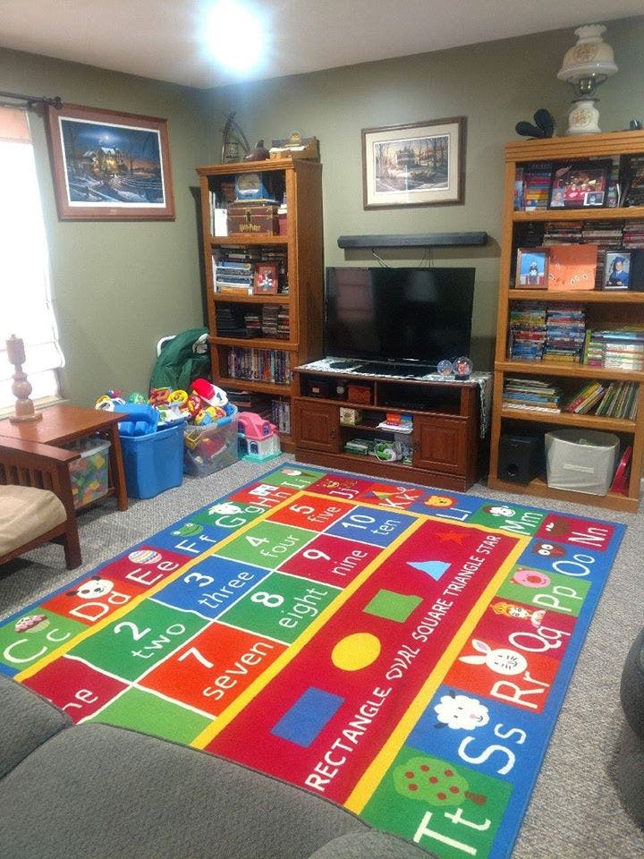 Living room with a colorful educational rug, bookshelves, and television