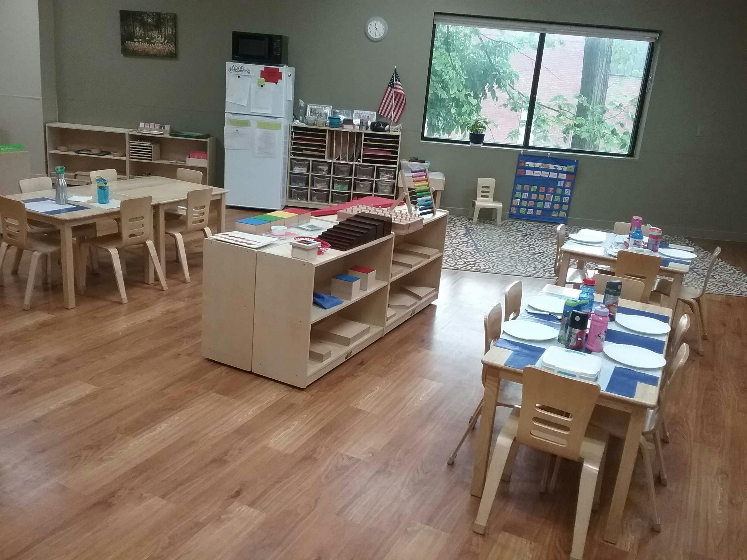 Classroom with small tables and chairs, shelves, and a large window