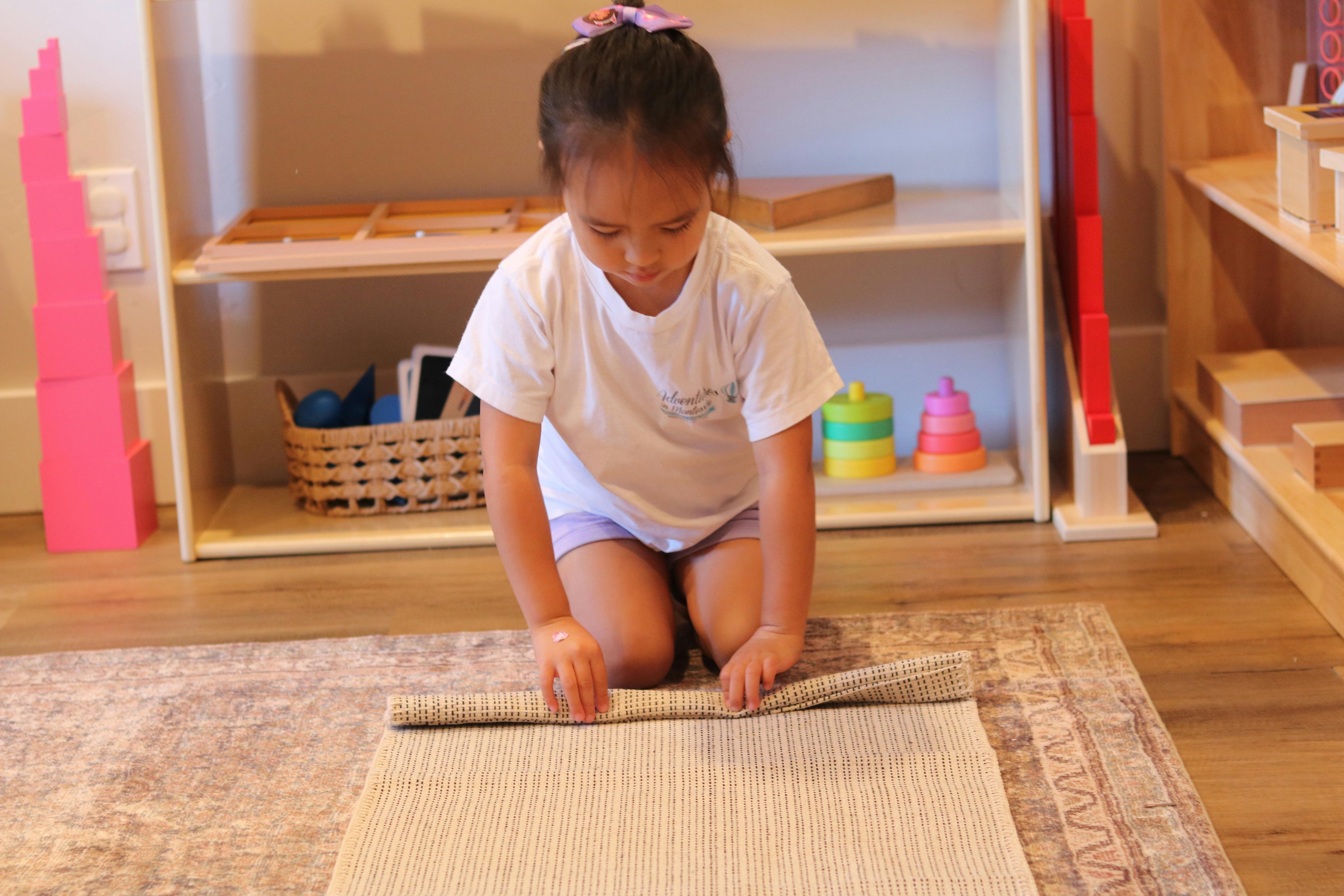 Child rolling up a mat on the floor