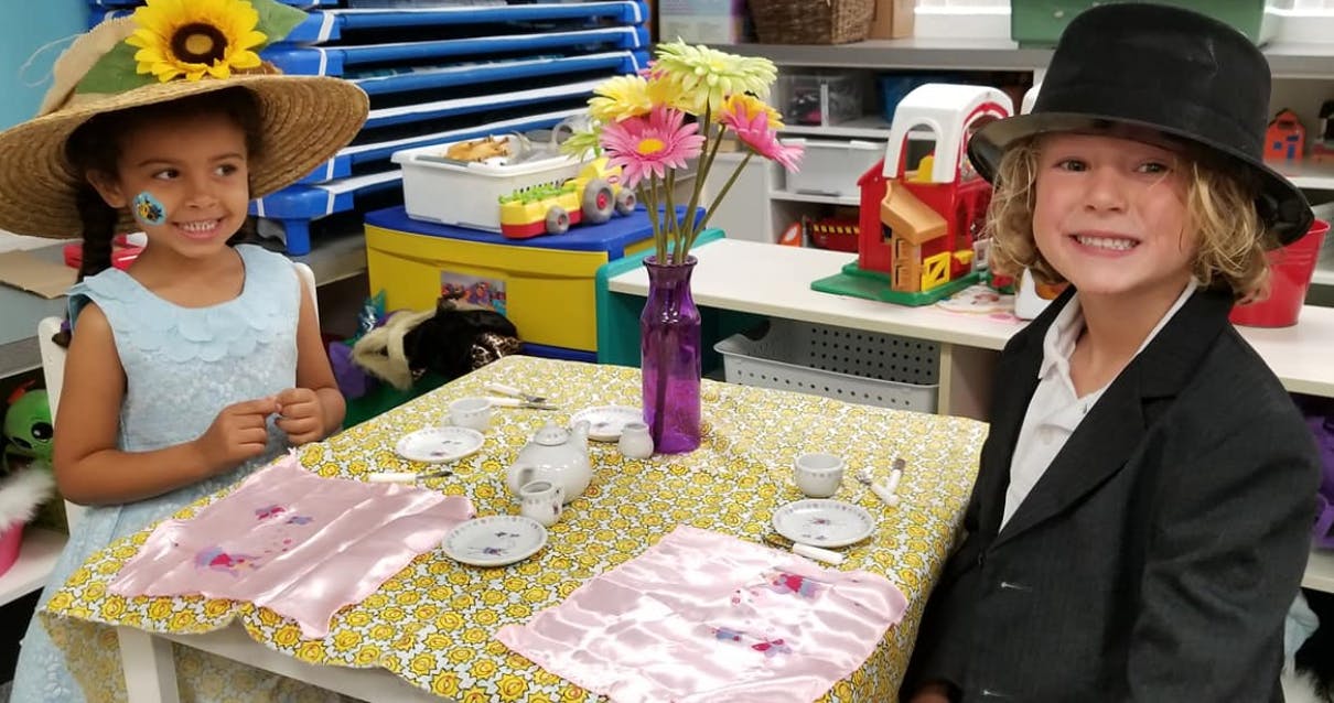 Two children at a table with a toy tea set and flowers