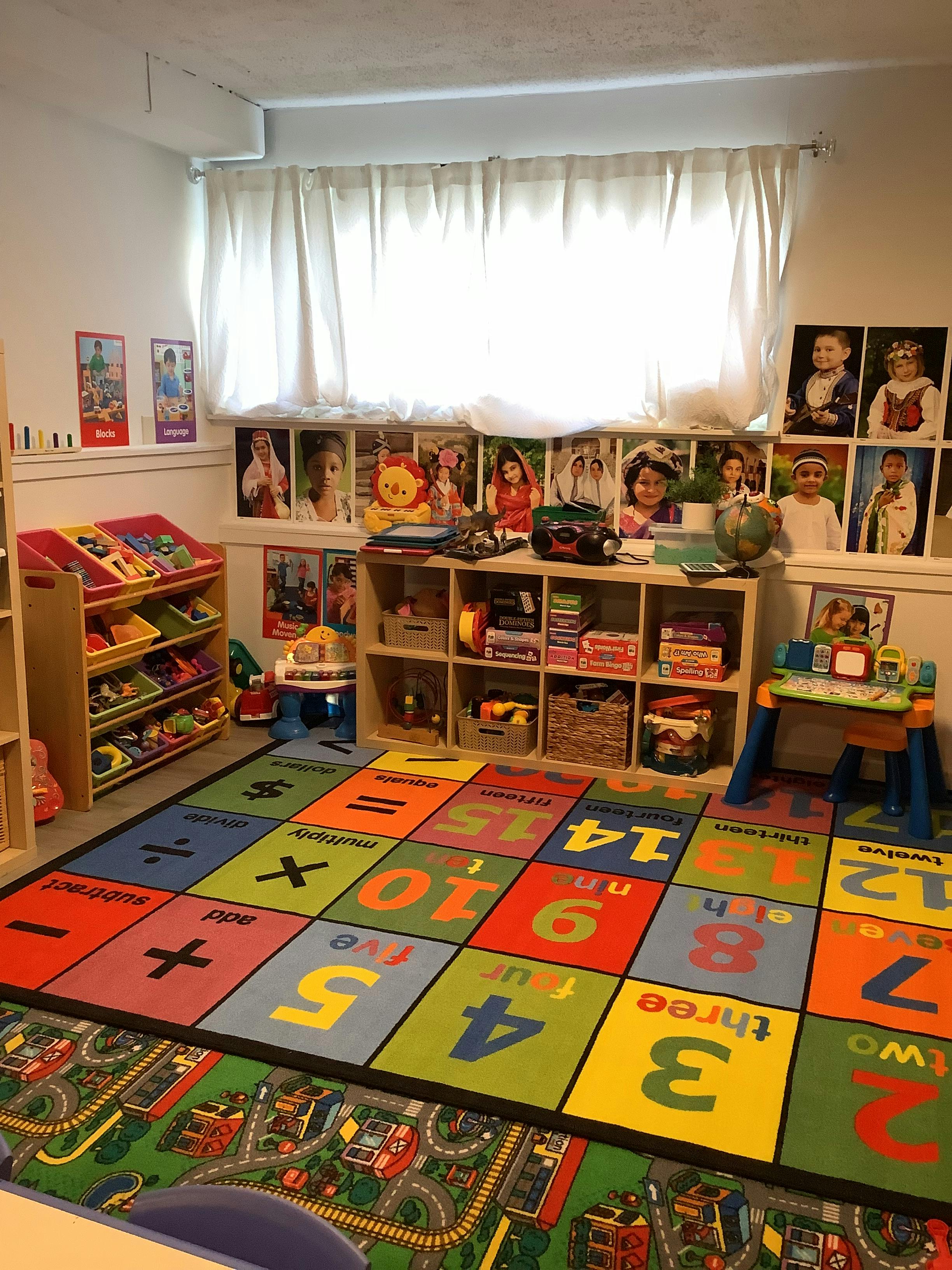 Playroom with colorful number rug, toy shelves, and window with white curtains