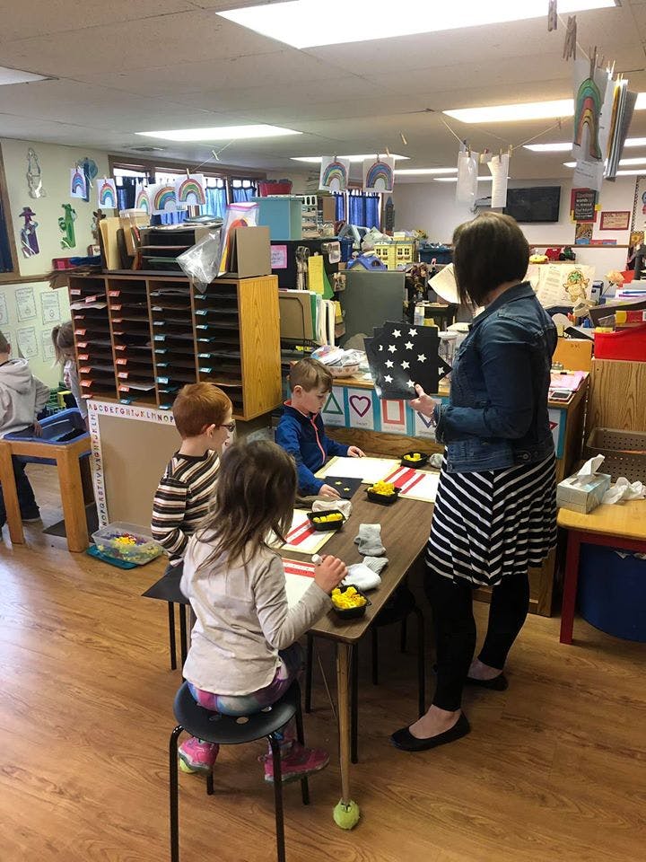 Adult showing a star-patterned board to children at a table in a classroom