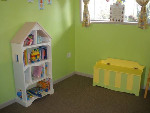 House-shaped bookshelf with books and toys next to a striped toy chest