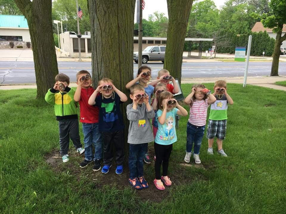 Group of children standing by a tree, looking through pretend binoculars