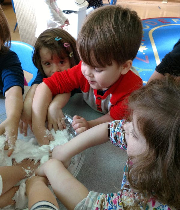 Children with hands in a bowl of white dough