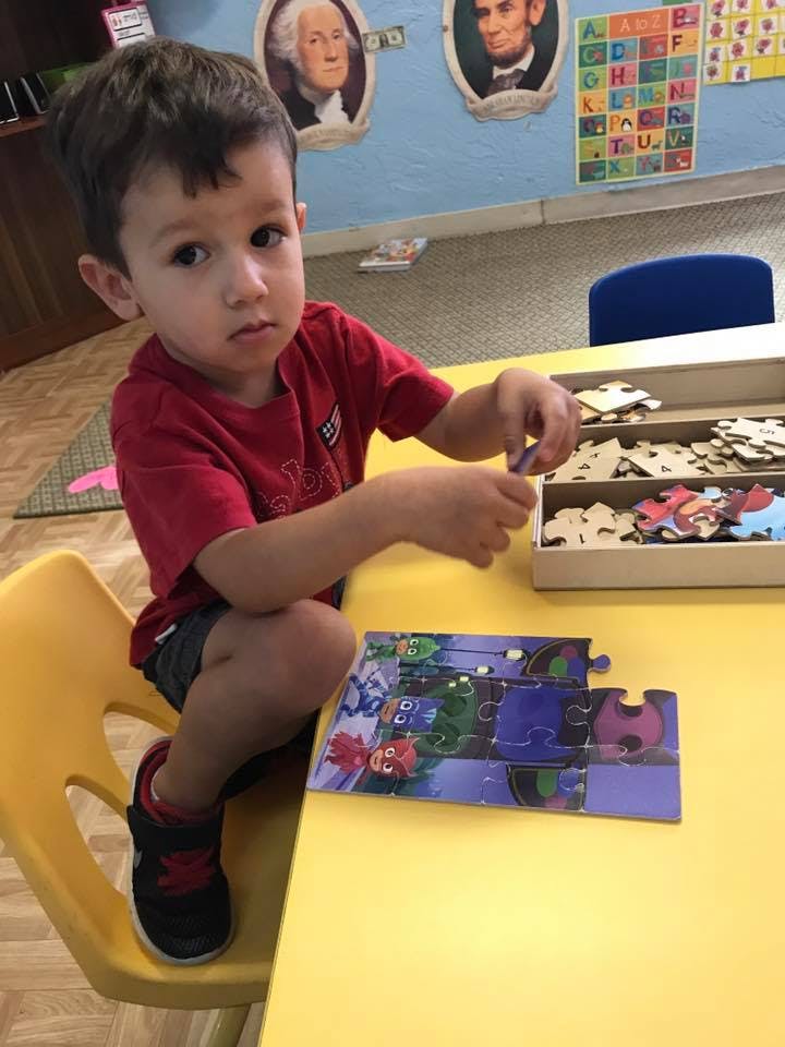 Child sitting at a table, working on a puzzle