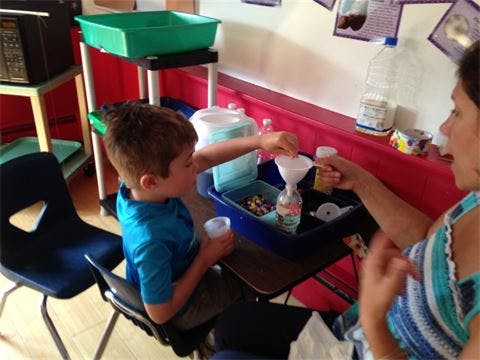 Child and person using a funnel to pour into a bottle