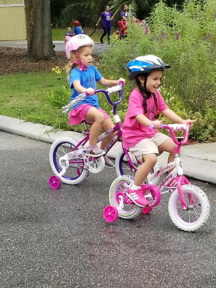 Two children wearing helmets riding bicycles with training wheels