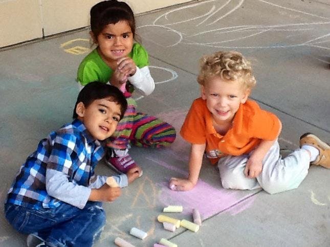 Three children drawing with chalk on the ground