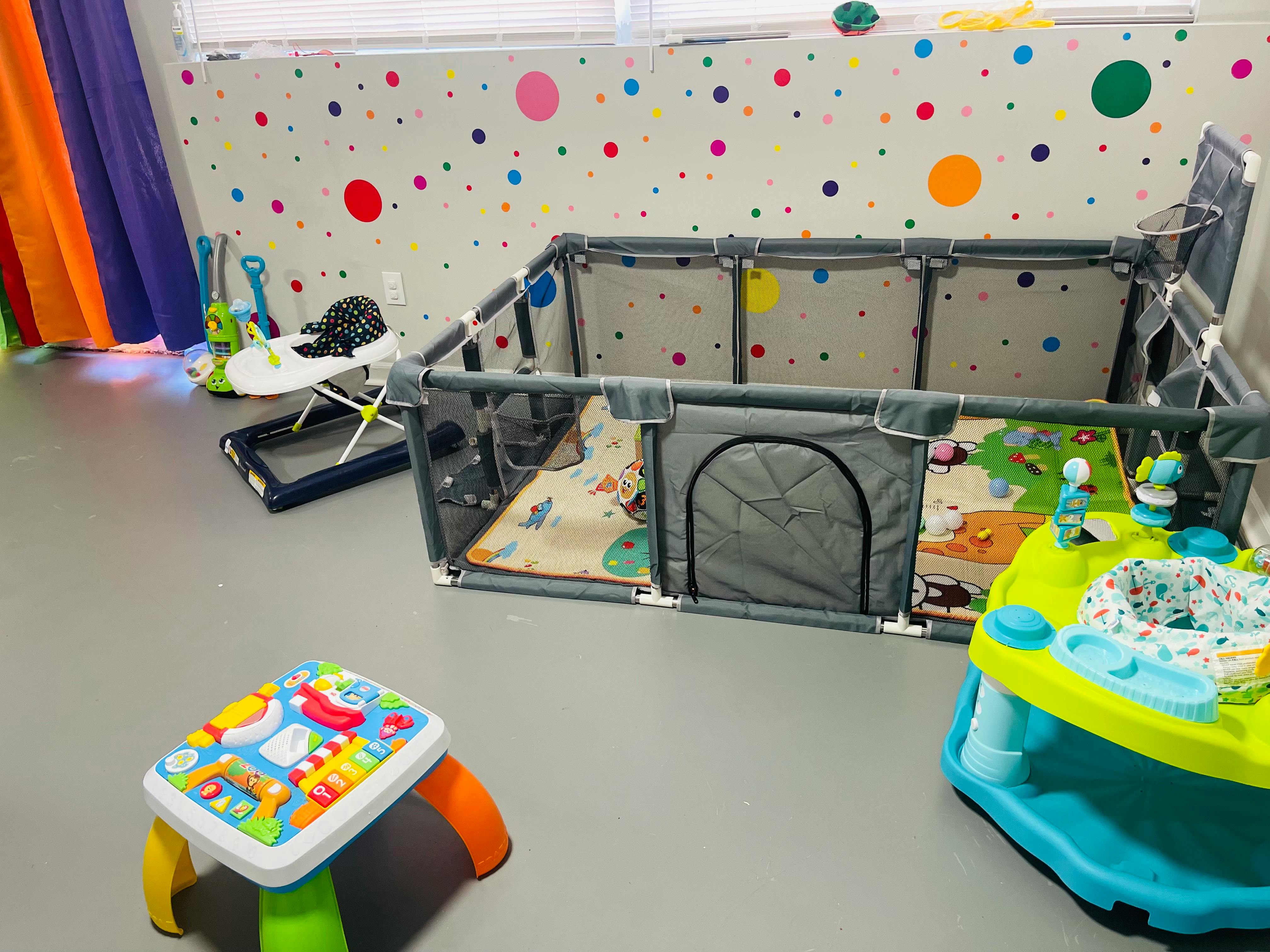 Playpen with a playmat inside and a baby walker nearby