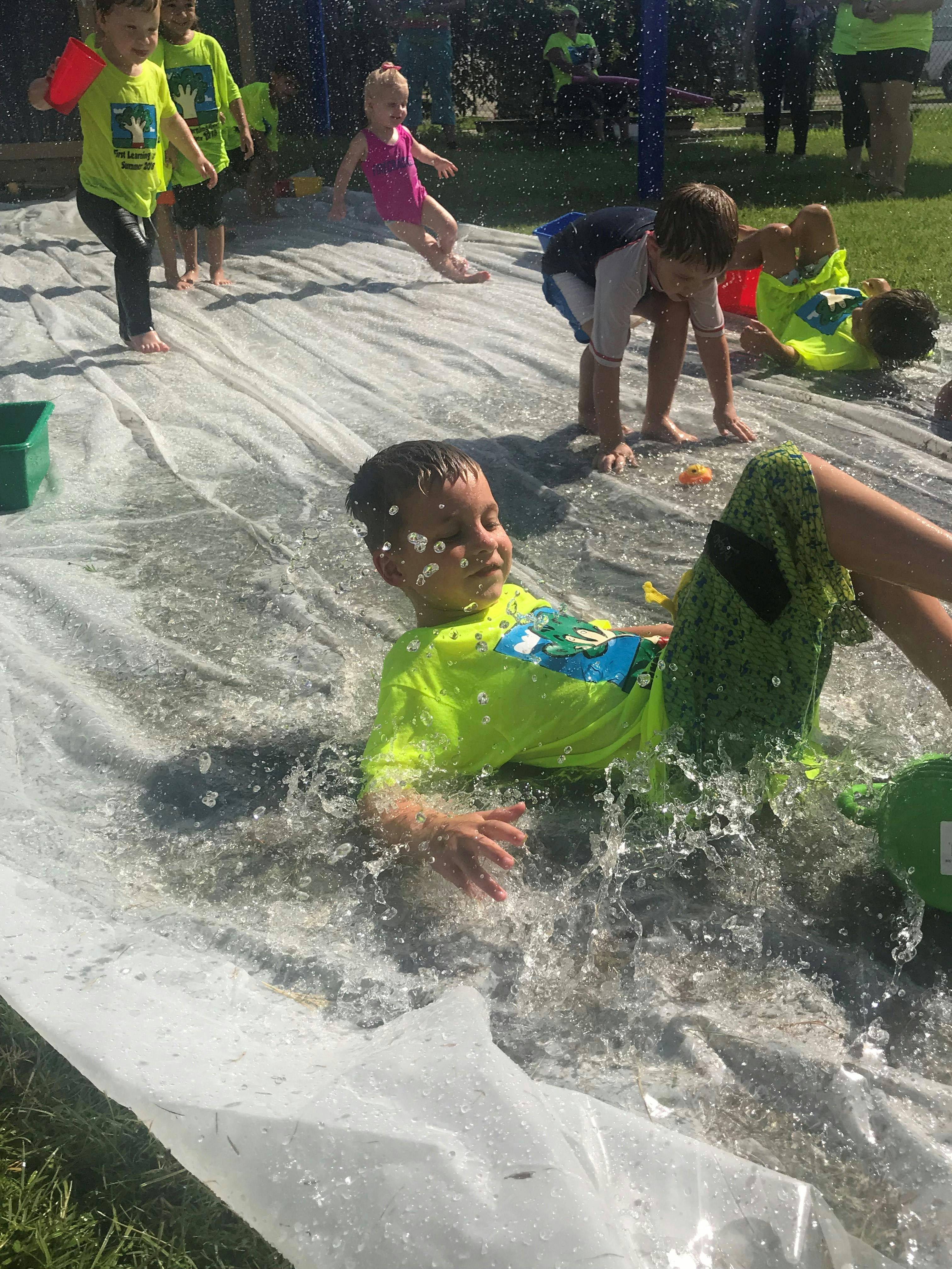 Child sliding on a wet plastic sheet with water splashing