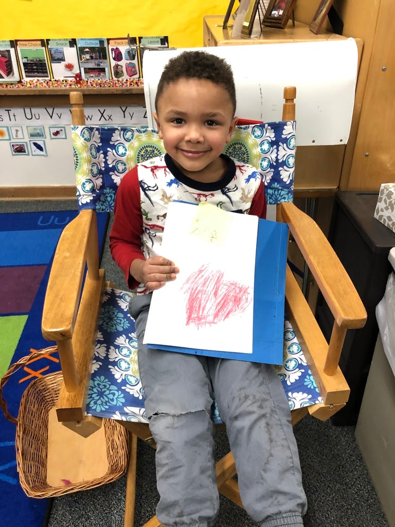 Child sitting in a chair holding up a drawing