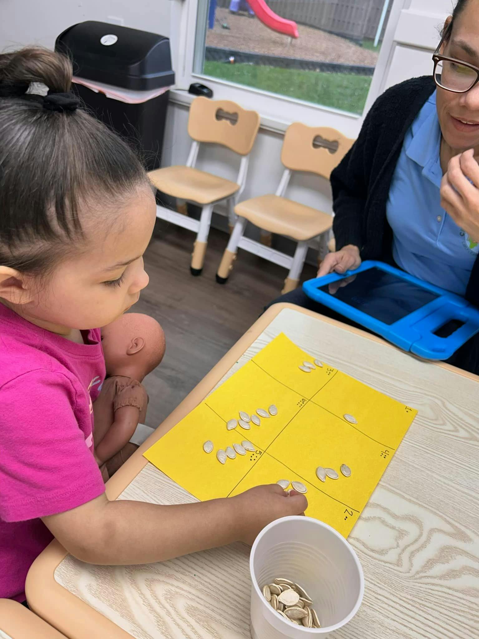 Child and person at a table with a yellow paper and seeds
