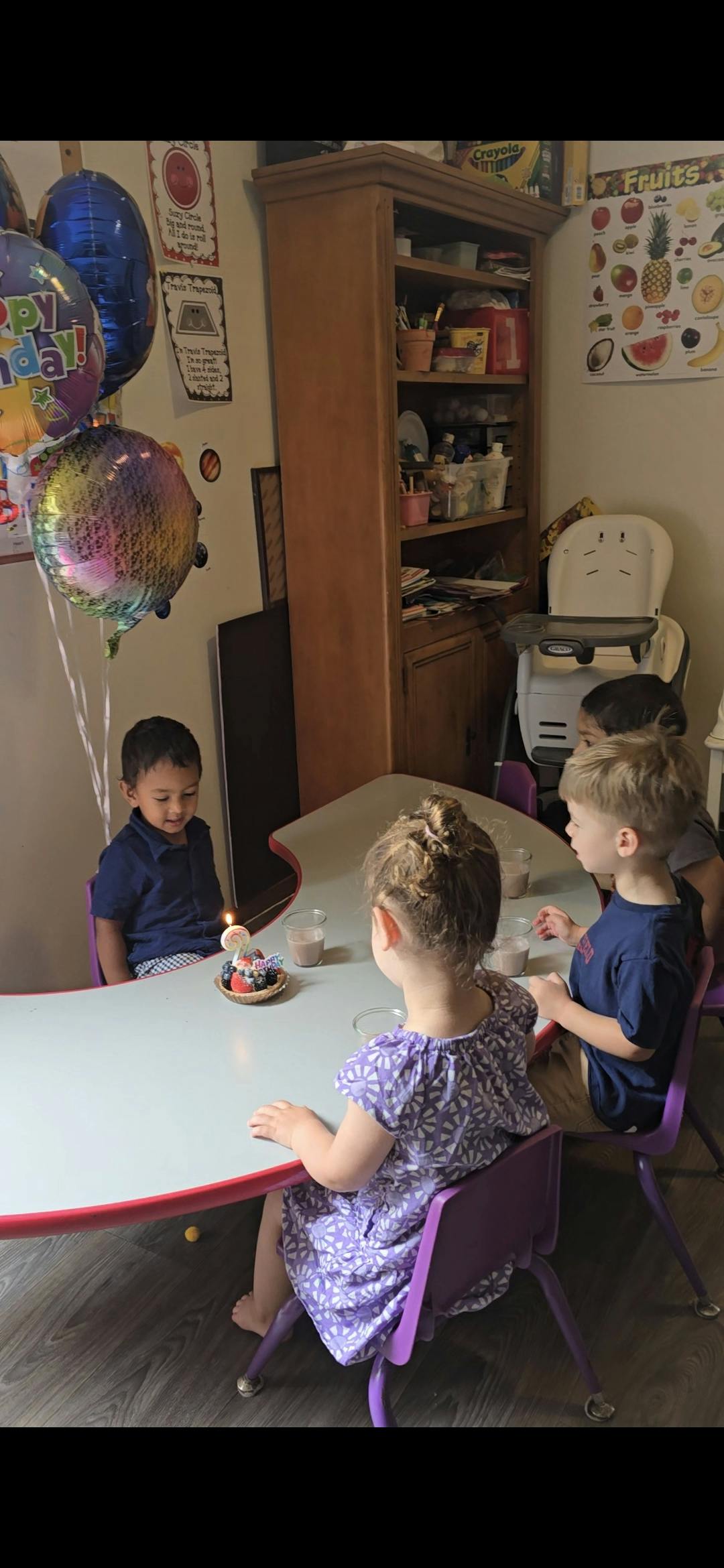 Children sitting at a table with a small cake and balloons