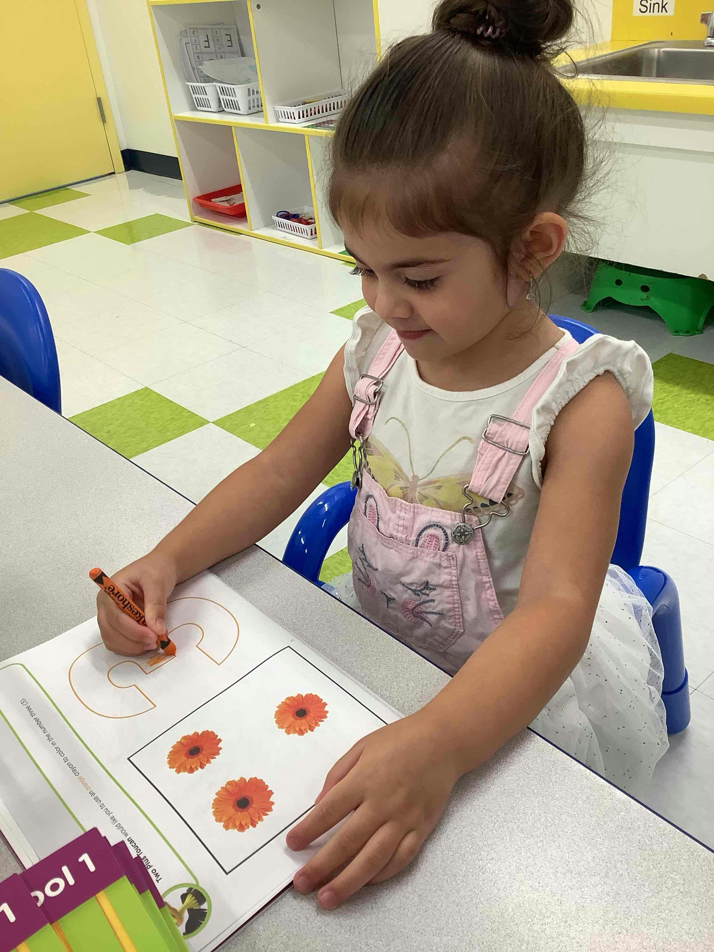 Child coloring a picture of flowers at a table in a classroom