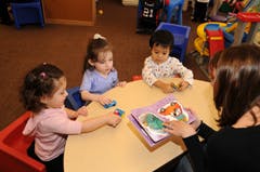 Adult and three children at a table with a book and toys