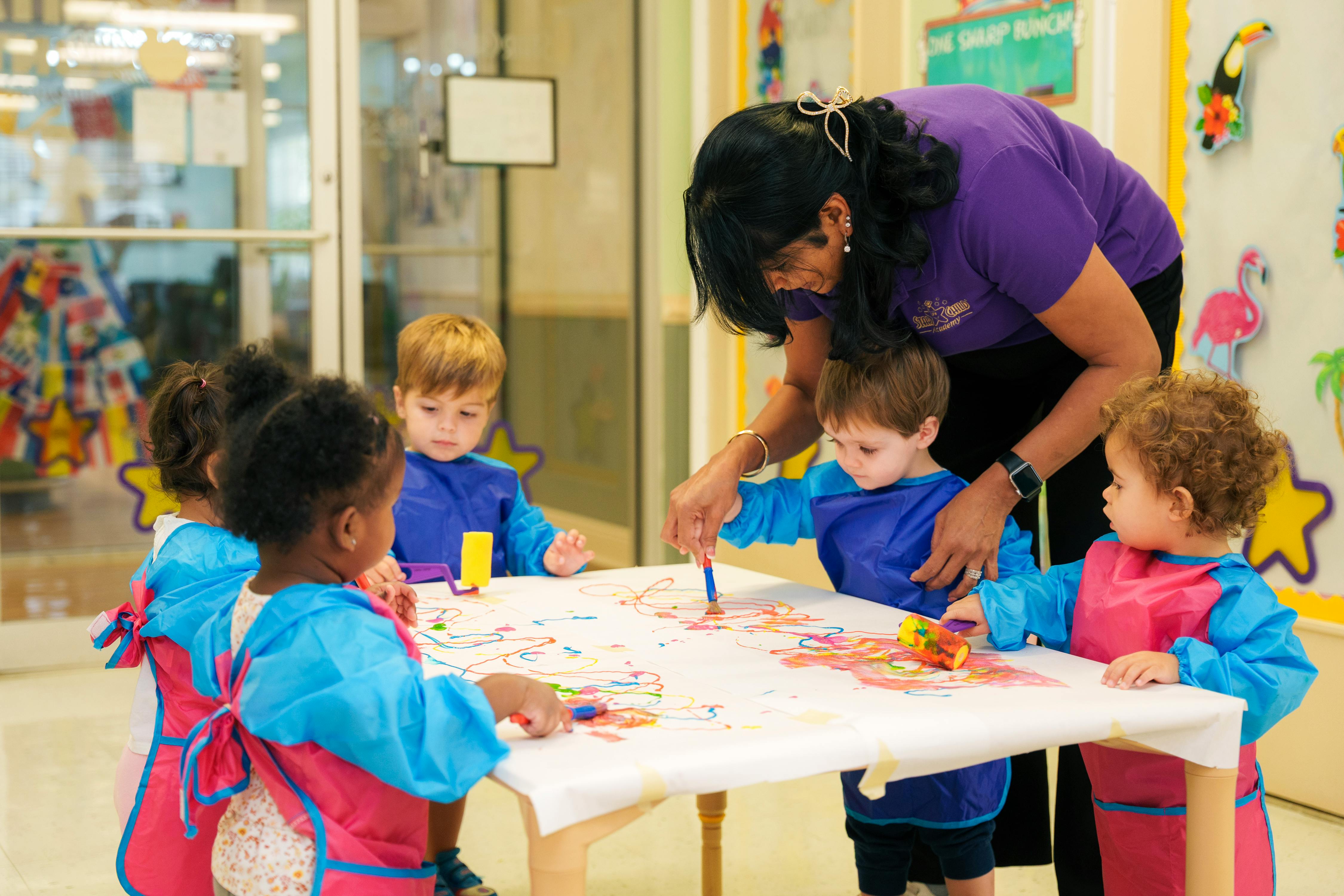 Adult and children painting at a table in a classroom