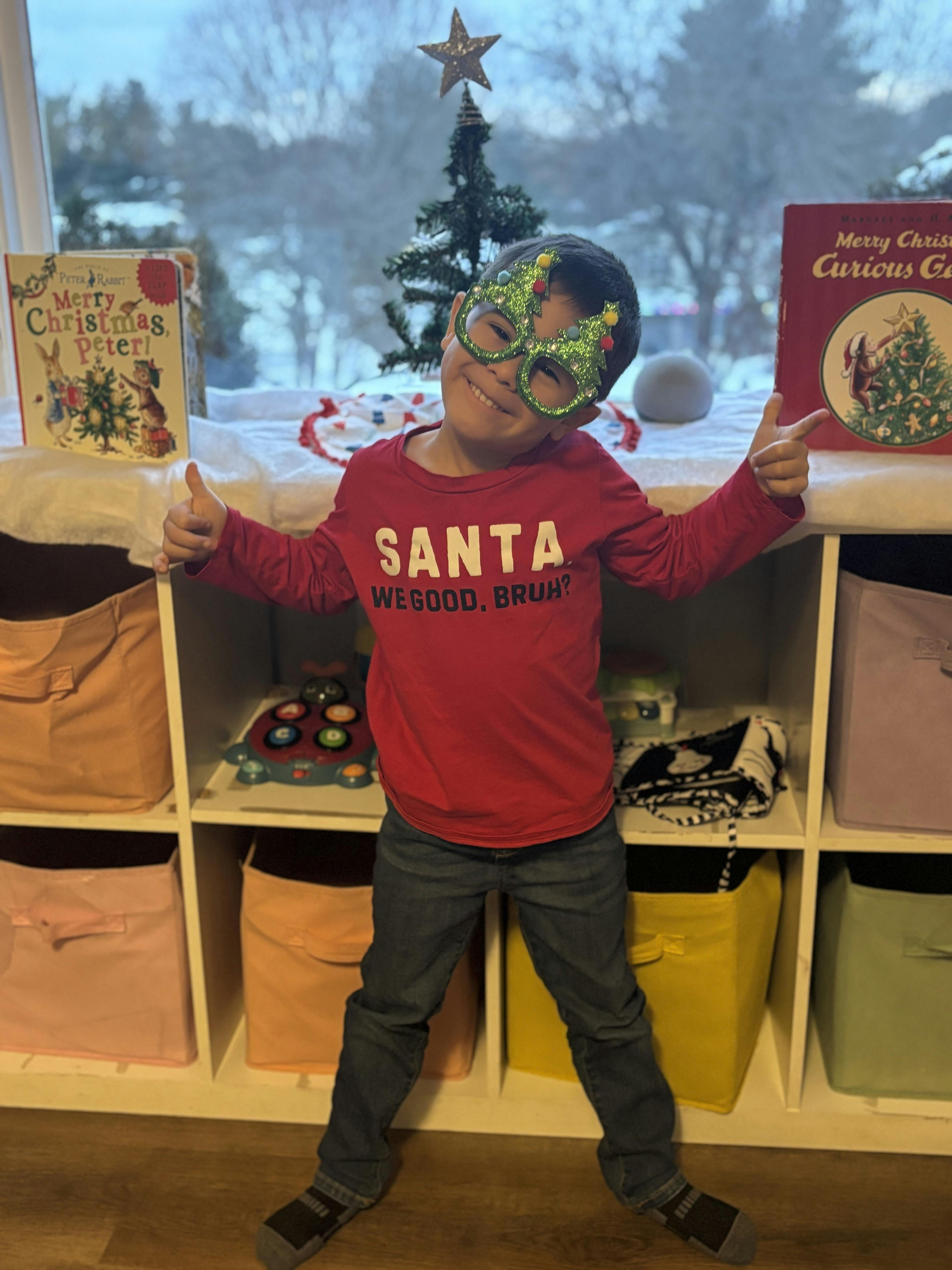 Child wearing Christmas tree glasses and a red shirt with "SANTA" on it