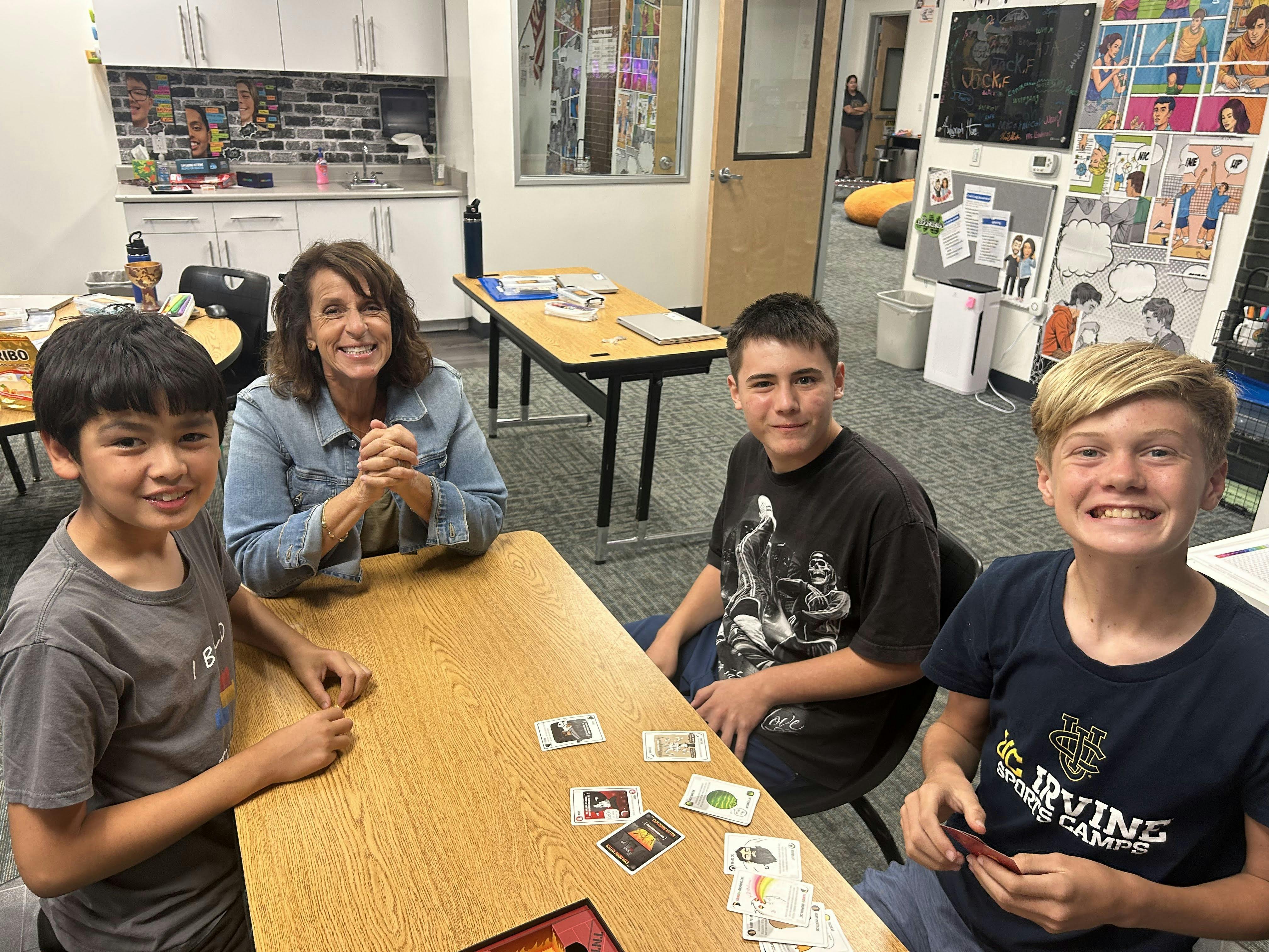 An adult and three teens playing a card game at a table in a classroom