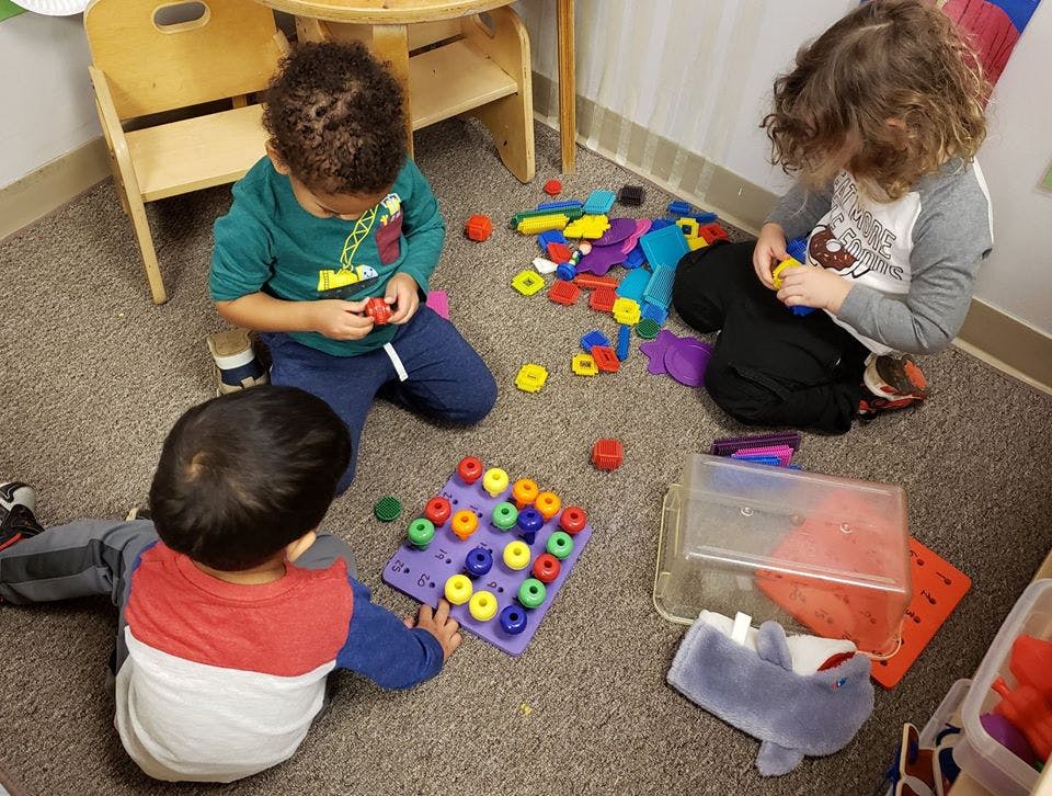 Three children playing with colorful toys on a carpeted floor