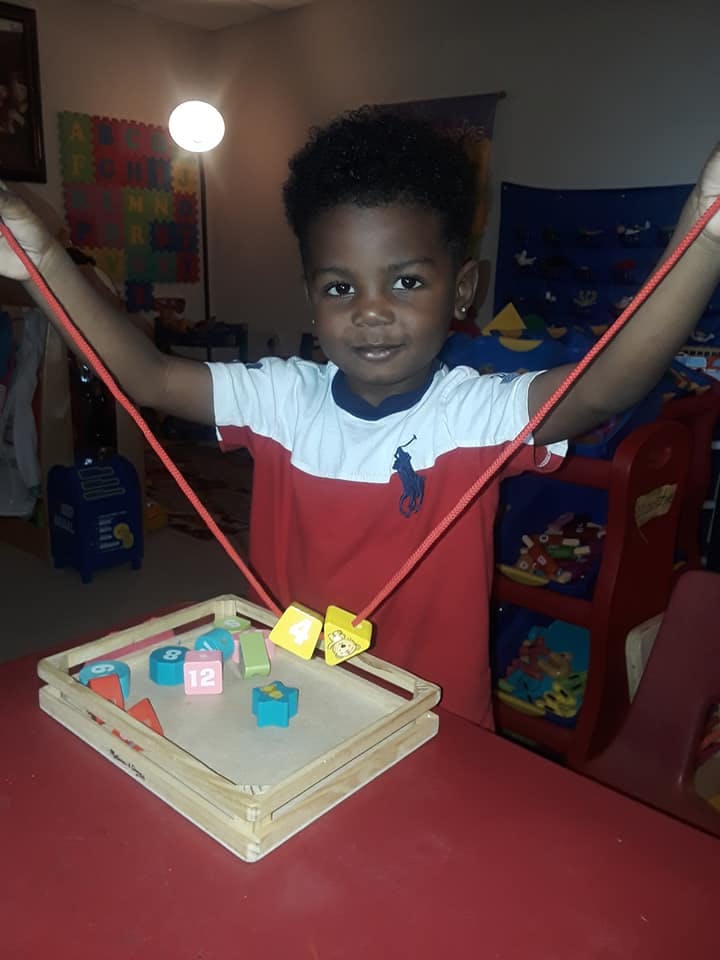 Child holding a string with beads over a wooden tray with blocks