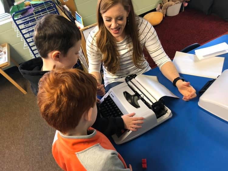 Adult and two children at a table with a braille typewriter