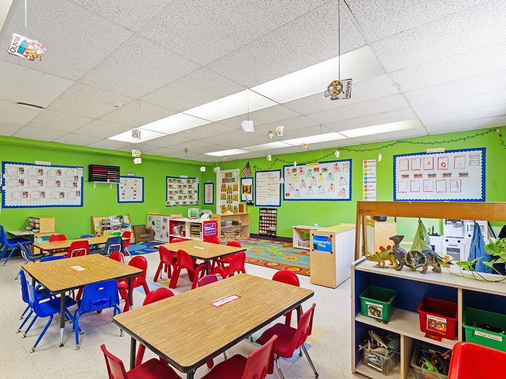 Classroom with green walls, small tables, and colorful chairs