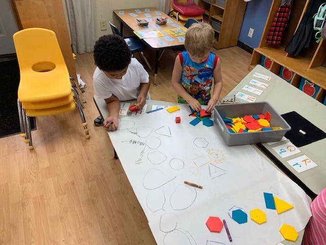 Two children playing with colorful shape blocks on a large sheet of paper